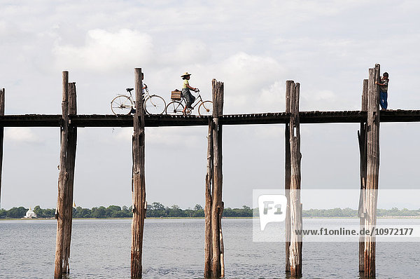 'Riding bicycles on an elevated wooden bridge over Taungthaman Lake; Amarapura  Myanmar'