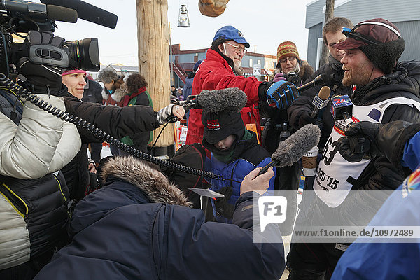 Radio and TV crews interview Aaron Burmeister shorlty after his arrival in third place at the Nome finish line during Iditarod 2015
