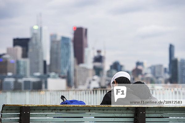 'Romantic couple is resting on a bench with skyscrapers in the background; Toronto  Canada'