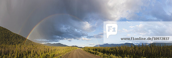Panorama eines doppelten Regenbogens und Regenwolken über einem unbefestigten Abschnitt des Alaska Highway in der Nähe des Kluane Lake  Yukon Territory  Kanada