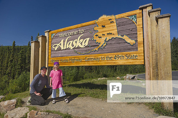 Mother and daughter pose beneath the Welcome to Alaska highway sign  Alaska Canada Boarder  Alaska  USA  Summer