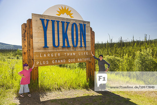 Mother and daughter pose beneath the Yukon Territory sign  Alaska Canada Boarder  Alaska  USA  Summer