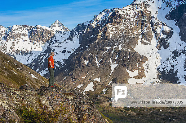 Wanderer auf einem Felsvorsprung mit Blick auf das Powerline Pass-Tal und den Wanderweg  Chugach State Park  Southcentral Alaska