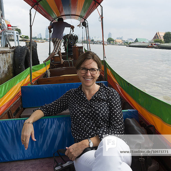 'A woman sitting on a tour boat along the river's shore; Bangkok  Thailand'