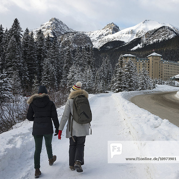 'Two young women walking on a snowy trail towards Chateau Lake Louise; Lake Louise  Alberta  Canada'