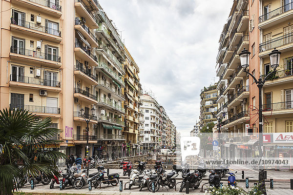 'Motorcycles parked at the end of a street with residential buildings and shops; Thessaloniki  Greece'