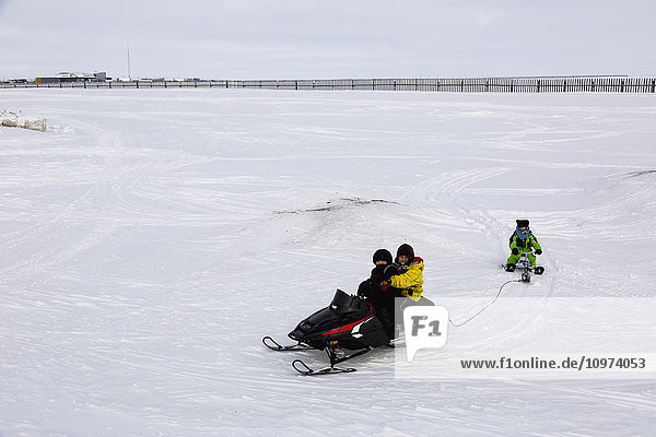 Einheimischer Alaska-Jugendlicher auf einer Schneemaschine  der einen anderen auf einem Schlitten hinter sich herzieht  Barrow  North Slope  Arctic Alaska  USA  Winter