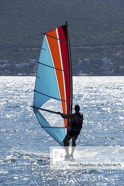 Windsurfen mit Sonnenlicht  das sich auf dem Wasser spiegelt  und Blick auf die Küste; Türkei'.