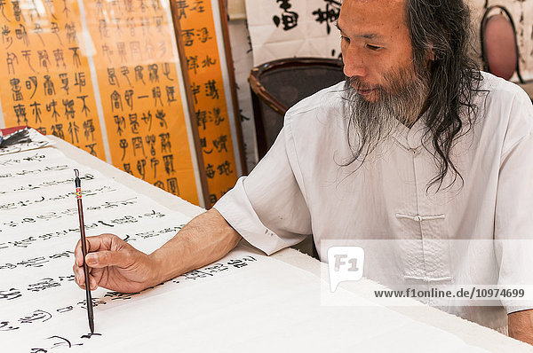 'A Chinese man writes characters in his street shop; Xian Shaanxi province China'
