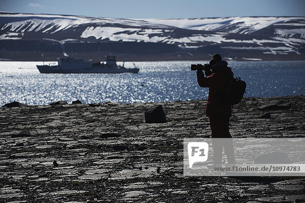 Silhouette eines Fotografen  der ein Schiff im Fjord fotografiert; Spitzbergen  Svalbard  Norwegen'.