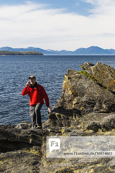 Ein Mann telefoniert mit seinem Smartphone an den felsigen Ufern der Tongass Narrows  Ketchikan  Südost-Alaska  Frühling