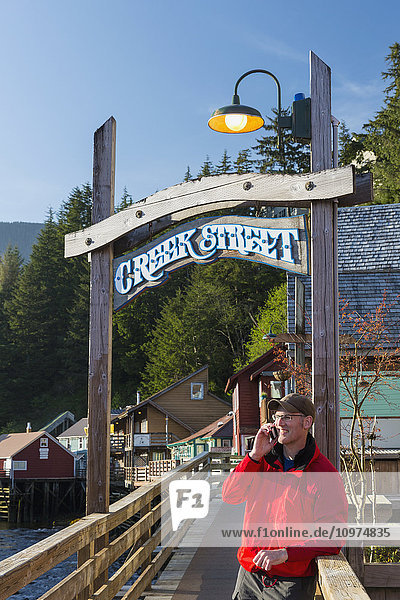 Mann am Handy in der Nähe des Creek Street-Schilds und der Promenade  Innenstadt von Ketchikan  Südost-Alaska  USA  Frühling