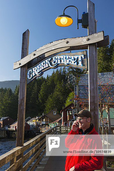 Mann am Handy in der Nähe des Creek Street-Schilds und der Promenade  Innenstadt von Ketchikan  Südost-Alaska  USA  Frühling