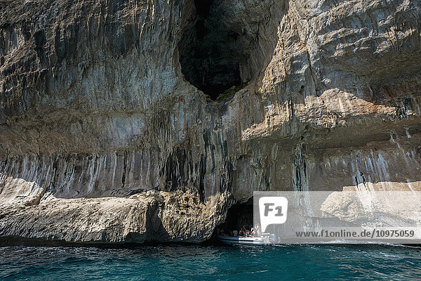 Ein Boot mit Touristen nähert sich einer Höhle an der Küste; Cala Gonone  Sardinien  Italien'.