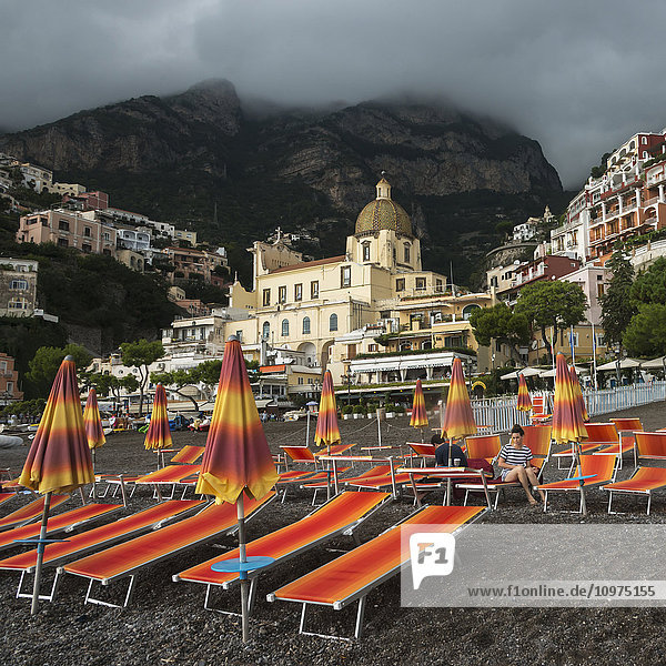Bunte Liegestühle am Strand mit Gebäuden im Hintergrund an der Amalfiküste; Positano  Kampanien  Italien'.