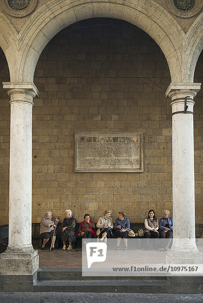 'A group of elderly women sit on a beach along a stone wall; Orvieto  Umbria  Italy'
