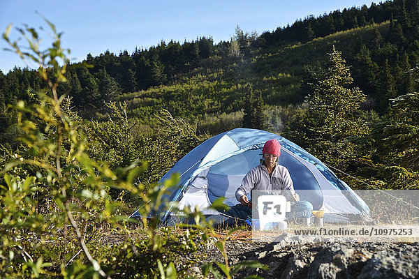 Eine Rucksacktouristin bereitet eine Mahlzeit im Camp in der Nähe des Upper Fuller Lake im Kenai National Wildlife Refuge auf der Kenai-Halbinsel in Süd-Zentral-Alaska zu.