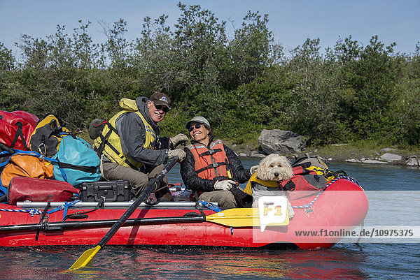 Ein Paar und sein Golden Doodle sitzen in einem Floß im Sonnenschein auf dem Marsh Fork des Canning River im Arctic National Wildlife Refuge  Sommer  Alaska