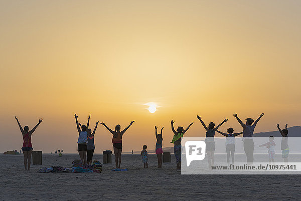 'A group of women with some children doing yoga on a beach at sunset; Tarifa  Andalusia  Spain'