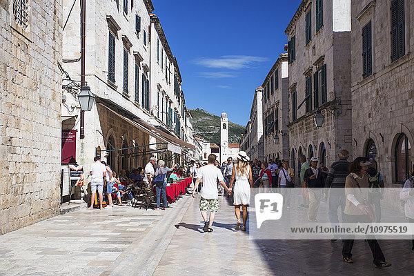 Menschen  die zwischen Gebäuden und Restauranttischen im Freien in der Altstadt von Dubrovnik spazieren gehen; Dubrovnik  Kroatien'.