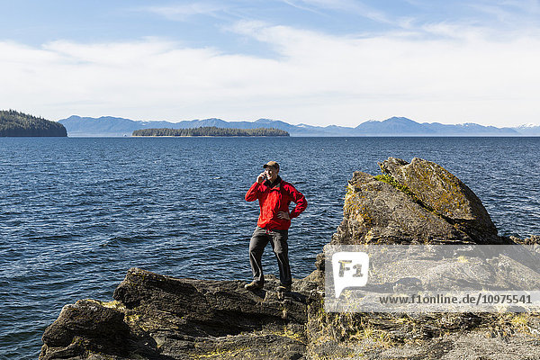Man talks on a cell phone on a cliff above Tongass Narrows near Ketchikan  Southeast Alaska  Spring