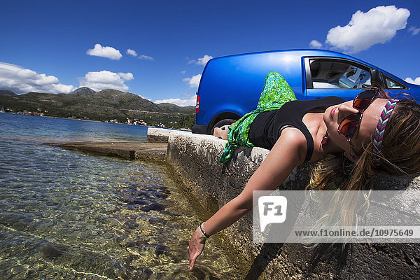 Eine junge Frau liegt auf einer Betonmauer an einem Strand an der Küste; Slano  Kroatien'.