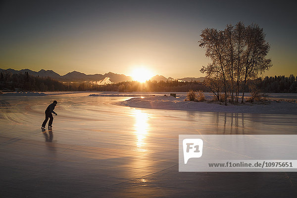 An ice skater skates on Westchester Lagoon at sunsrise in midtown Anchorage  Southcentral Alaska  winter