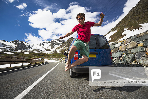'A young man jumps in the air on a mountain pass road in the Western Alps; Italy'