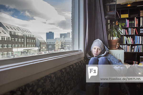 'A girl sits on the floor of an apartment with a view out the window; Reykjavik Iceland'