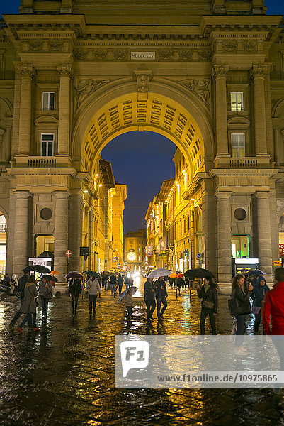 'Pedestrians on a wet walkway at nighttime with illuminated buildings; Florence  Toscana  Italy'