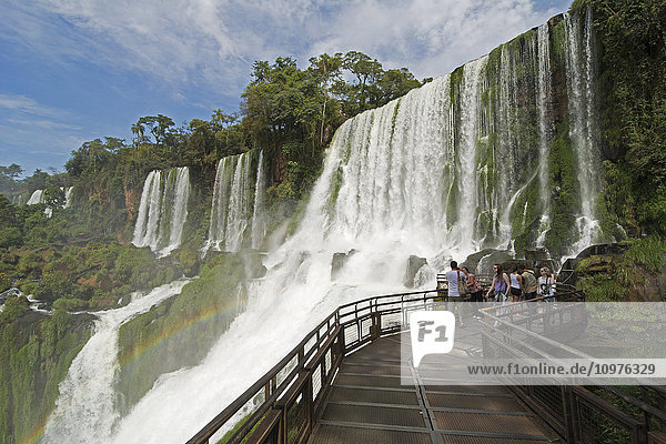 'Metal walkway leading to Iguazu Falls  with a rainbow is visible over the water; Missiones  Argentina'