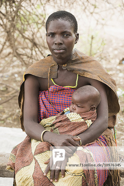 Datoga-Mutter in traditioneller Kleidung hält ihr Baby auf dem Schoß in der Nähe des Eyasi-Sees; Tansania'.