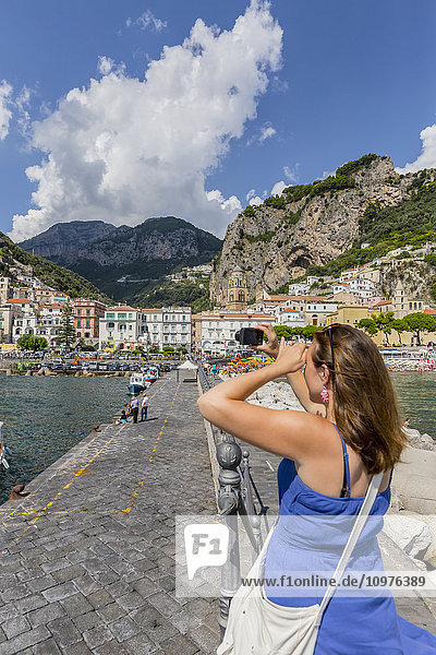 Eine Touristin fotografiert die italienische Stadt Amalfi von der Uferpromenade am Mittelmeer aus; Amalfi  Provinz Salerno  Italien'.