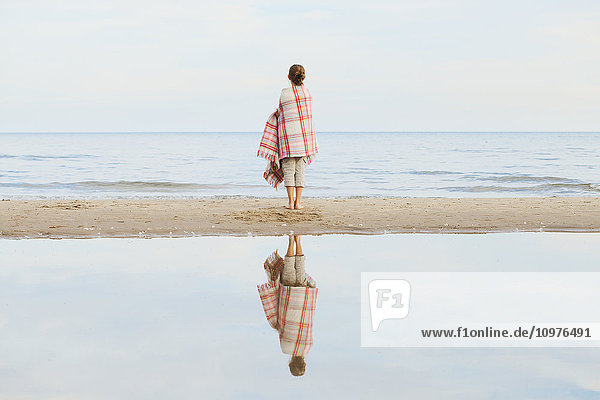 Mädchen  das sich im Wasser spiegelt und in eine Decke eingewickelt am Strand steht; Toronto  Ontario  Kanada'.
