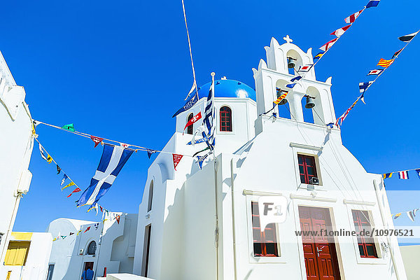 Eine traditionelle griechisch-orthodoxe Kirche mit Weltflaggen  die in allen Richtungen zur Feier des Tages wehen  und der griechischen Flagge; Oia  Santorin  Griechenland'
