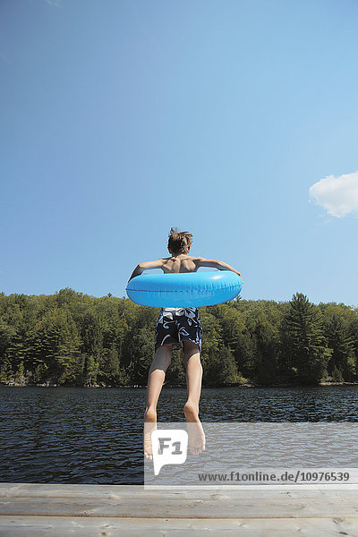 Junge mit aufblasbarem Ring springt vom Ende des Stegs am Crystal Lake; Ontario  Kanada'.