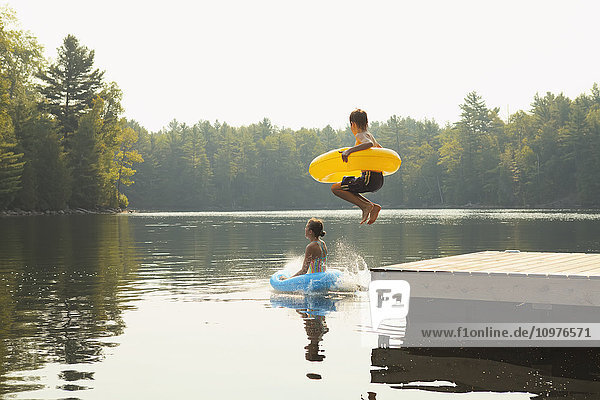 'Kids jumping off end of dock holding inflatable rings on Crystal Lake; Ontario  Canada'