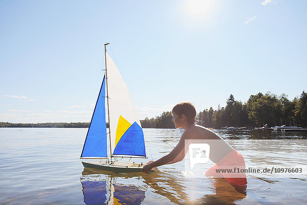 Junge steht im See und spielt mit einem Segelboot; Ontario  Kanada'.