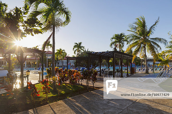Die Sonne geht durch die Palmen unter und wirft lange Schatten auf das Pooldeck in diesem Resort in Kuba; Varadero  Kuba