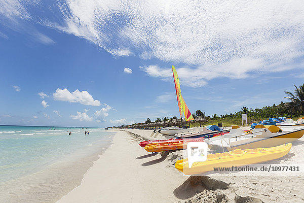 Blick auf den weißen Sandstrand an einem sonnigen Tag mit Kajaks und Booten  die im Sand liegen  und Menschen im Meer in der Ferne; Varadero  Kuba