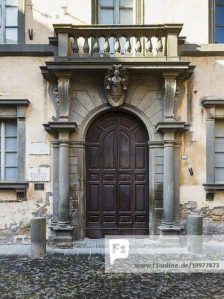 Holzbogentür und Säulen mit einem kleinen Balkon an einem Wohnhaus; Orvieto  Umbrien  Italien'.