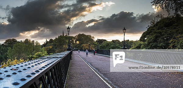 Fußgänger und ein Läufer auf einer Brücke mit leuchtenden Wolken bei Sonnenuntergang; Newcastle  Tyne and Wear  England'.