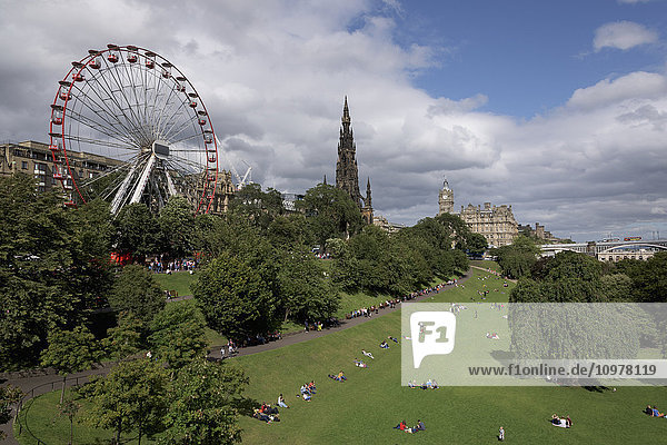 'People sitting on the grass enjoying the sunshine with a ferris wheel behind them; Edinburgh  Scotland'