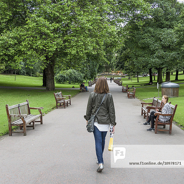 Eine Frau geht einen mit Bänken und Bäumen gesäumten Weg in den Princes Street Gardens entlang; Edinburgh  Schottland'.