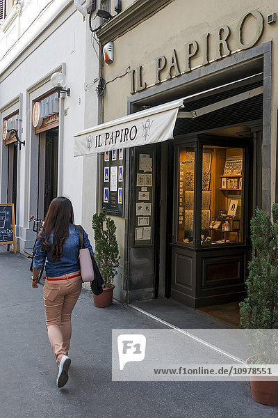 Eine junge Frau geht an einem Geschäft mit Schaufensterauslage vorbei; Florenz  Italien'.