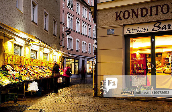 Ein Geschäft und ein Markt im Freien  beleuchtet in der Abenddämmerung; Regensburg  Bayern  Deutschland'.