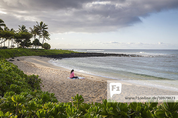 Eine junge Frau arbeitet am frühen Morgen an ihrem Computer am Strand; Poipu  Kauai  Hawaii  Vereinigte Staaten von Amerika