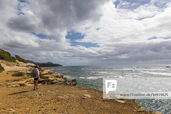 Ein Wanderer steht auf einer Klippe und beobachtet einen herannahenden Regensturm; Poipu  Kauai  Hawaii  Vereinigte Staaten von Amerika'.
