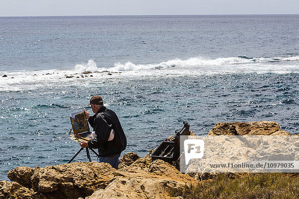 Ein Mann am Meeresufer malt eine Küstenszene von einer Staffelei aus; Poipu  Kauai  Hawaii  Vereinigte Staaten von Amerika'.
