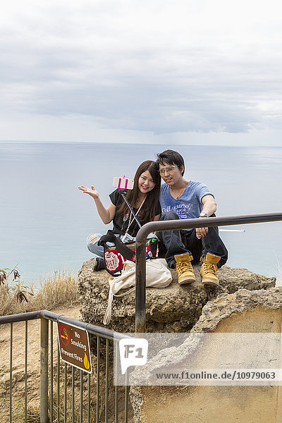Ein junges Paar macht ein Selfie-Foto mit einem Selfie-Stick und einem intelligenten Foto auf Diamond Head; Oahu  Hawaii  Vereinigte Staaten von Amerika'.